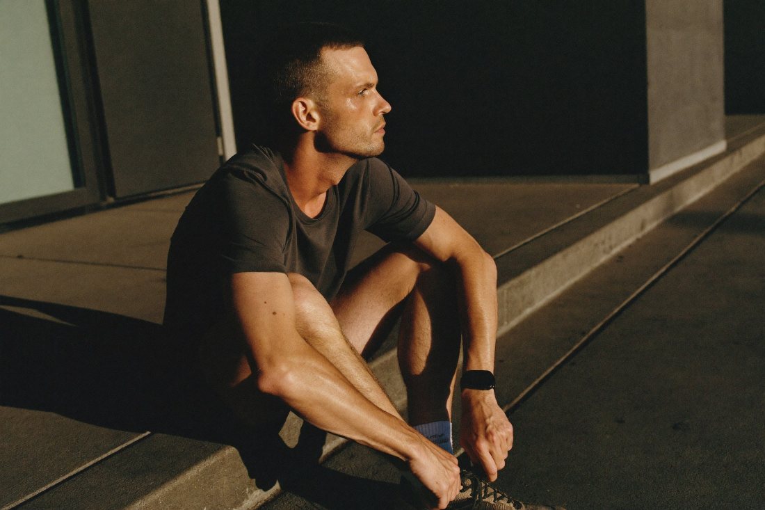 A man sitting on a step in low afternoon light, loosening a shoe after a run.